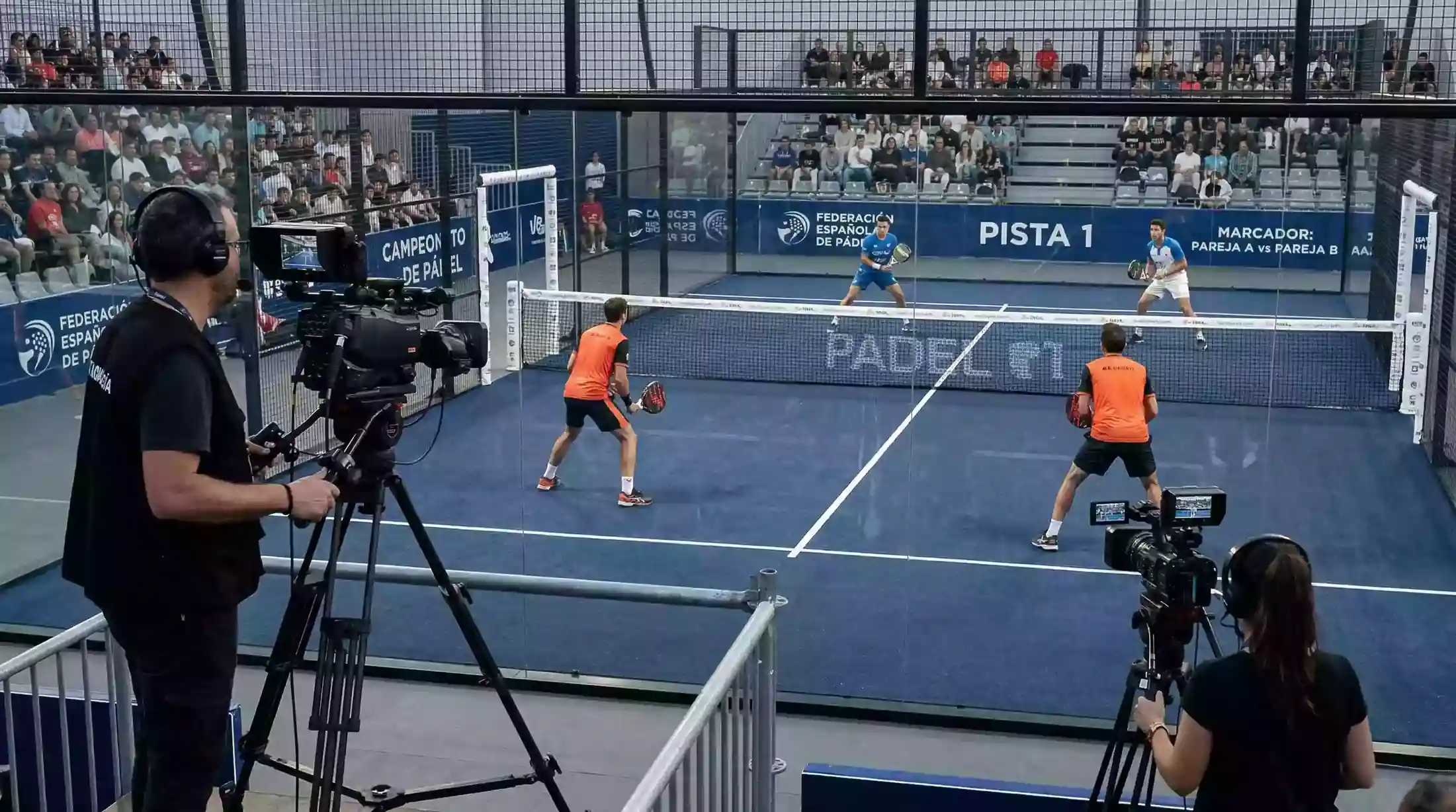 Cámaras de televisión retransmitiendo un partido de pádel profesional en una pista de cristal